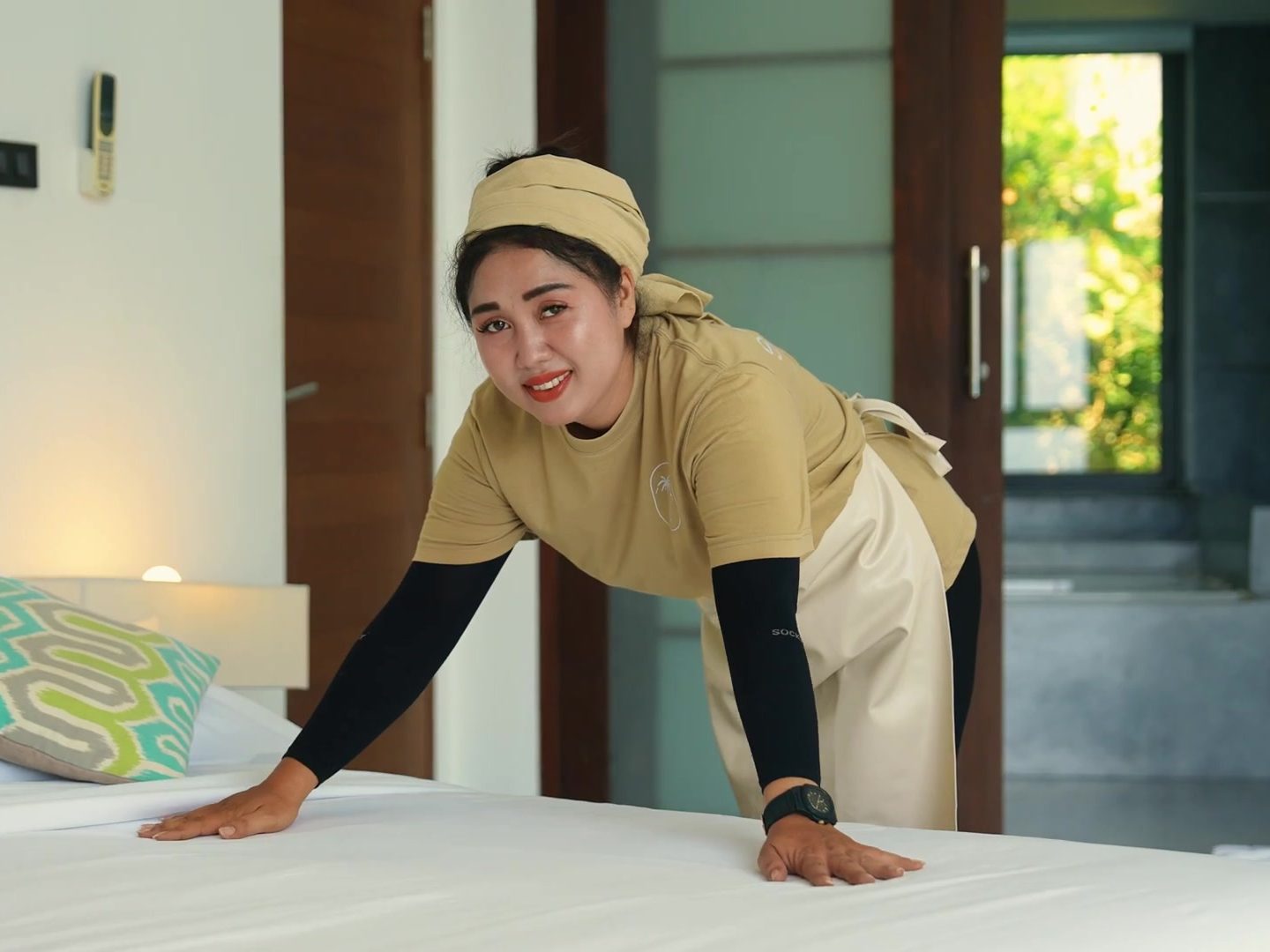 A Staylar housekeeper making up a bed in a villa bedroom